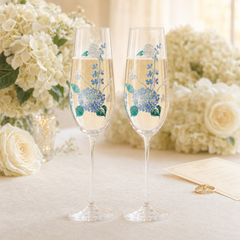 Pair of hand-painted blue hydrangea champagne flutes displayed in an elegant floral celebration setting