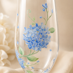 Close-up of hand painted blue hydrangea flowers and green leaves on champagne glass