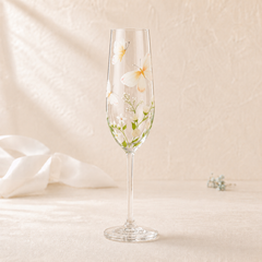 Hand-painted butterfly champagne flute with white wildflowers and green botanical details on a soft ivory background